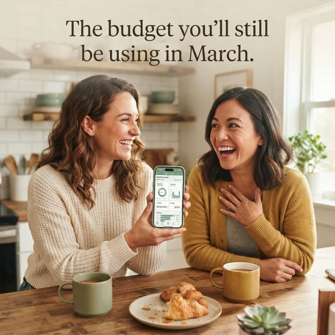 Two women at a kitchen table looking at the budget dashboard on a phone together